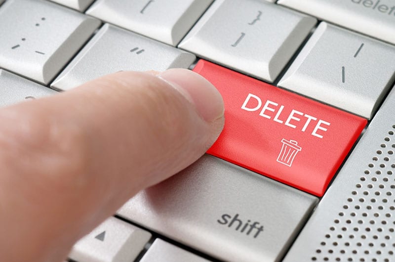 A finger hits a red delete button on a computer keyboard